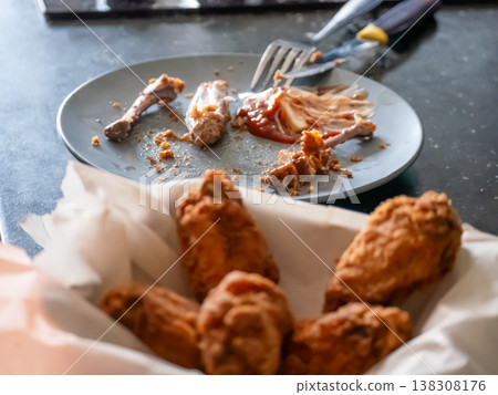 Man eating deep-fried chicken wings from a paper basket. Crispy appetizer served at home. Casual meal, hungry person enjoying fast food snack. Delicious culinary experience and diet concept. 138308176