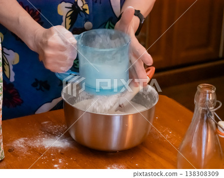 Woman sifting flour into metal bowl in kitchen. Baker preparing dough for cake or bread. Homemade pastry process. Domestic food hobby, culinary activity for baking cake and muffin. Woman sifting flour into metal bowl in kitchen. Baker preparing dough for cake or bread. Homemade pastry process. Domestic food hobby, culinary activity for baking cake and muffin. 138308309