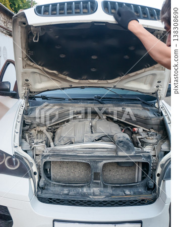 Mechanic opening white car hood for engine inspection. Professional technician checking vehicle motor for diagnostic repair. Automotive maintenance service in service station workshop. 138308690