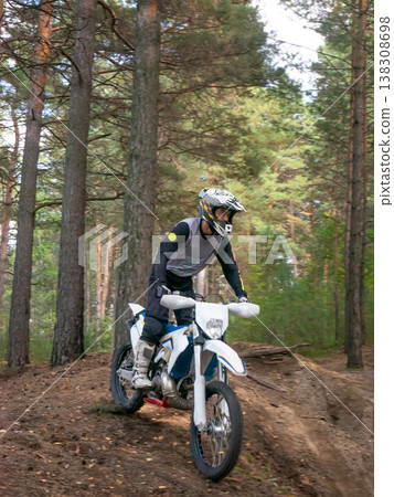 Motorcyclist riding dirt bike through pine forest. Biker in protective gear driving off-road motorcycle on trail. Extreme sport activity and active hobby in nature during summer day. 138308698