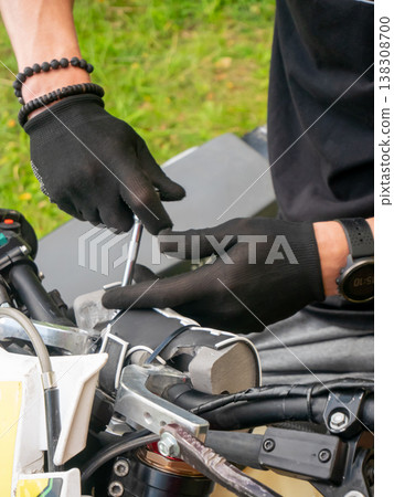 Mechanic repairing motorcycle handlebar with tool. Man fixing motorbike controls using screwdriver. Outdoor vehicle maintenance, technical service, restoration and garage hobby project work. Mechanic repairing motorcycle handlebar with tool. Man fixing motorbike controls using screwdriver. Outdoor vehicle maintenance, technical service, restoration and garage hobby project work. 138308700