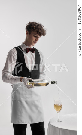 Waiter in formal uniform pouring white wine into glass in studio setting. Waiter in formal uniform pouring white wine into glass in studio setting. 138308964
