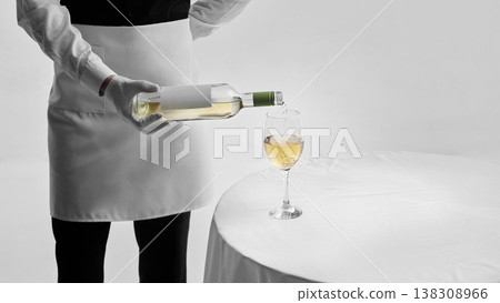 Waiter in formal uniform pouring white wine into glass on table in studio. Waiter in formal uniform pouring white wine into glass on table in studio. 138308966