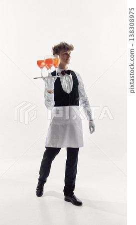 Waiter in formal uniform walking while carrying tray with orange cocktails in studio Waiter in formal uniform walking while carrying tray with orange cocktails in studio 138308975