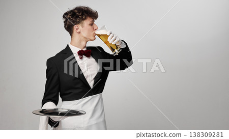Waiter drinking beer in formal uniform with tray in minimal studio setting Waiter drinking beer in formal uniform with tray in minimal studio setting 138309281