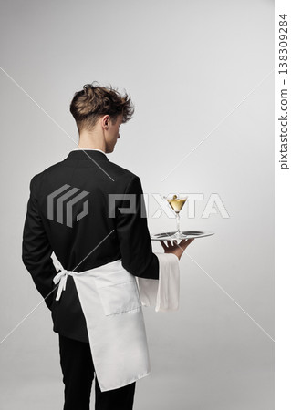 Waiter holding cocktail tray while looking down in minimal studio portrait. Waiter holding cocktail tray while looking down in minimal studio portrait. 138309284