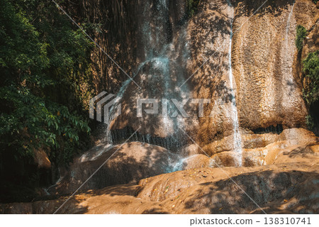 Sai Yok Noi waterfall flowing over textured rocks in tropical forest with sunlight and shadows, Scenic natural cascade in lush jungle environment, tranquility and travel destinations of Thailand 138310741