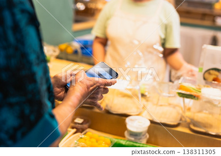 Senior woman using a smartphone paying bill at desert store. Senior woman using a smartphone paying bill at desert store. 138311305