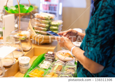 Senior woman using a smartphone paying bill at desert store. Senior woman using a smartphone paying bill at desert store. 138311306