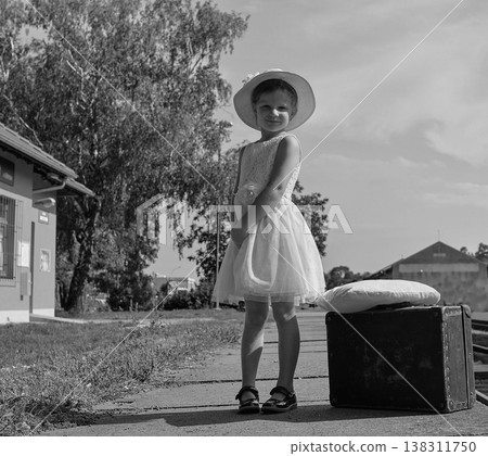 Young girl in a dress and hat with a suitcase at a train station, vintage style Young girl in a dress and hat with a suitcase at a train station, vintage style 138311750