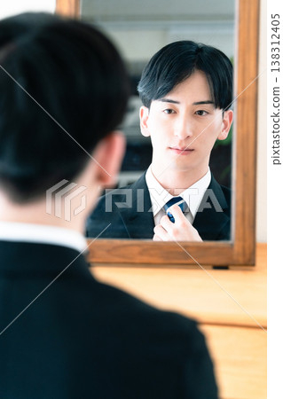 A man in a suit tying his tie in front of a mirror. 138312405