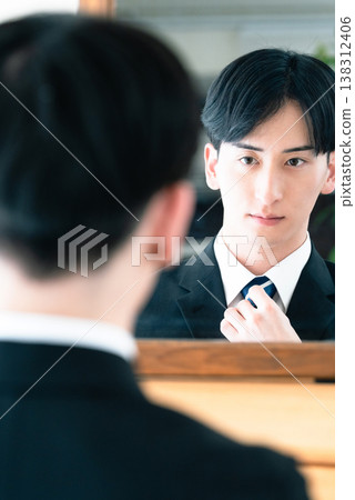 A man in a suit tying his tie in front of a mirror. A man in a suit tying his tie in front of a mirror. 138312406