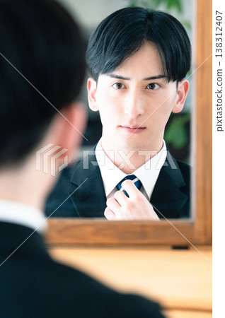 一個身穿西裝的男人正在鏡子前繫領帶。 138312407
