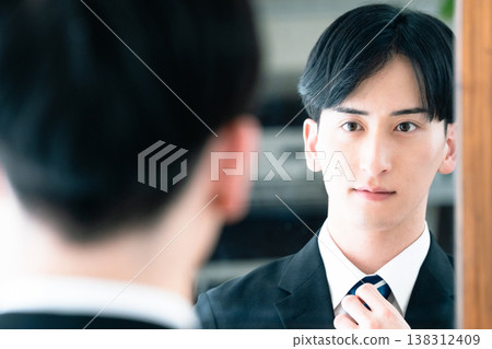 A man in a suit tying his tie in front of a mirror. A man in a suit tying his tie in front of a mirror. 138312409