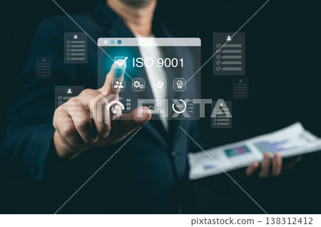 Businessman in suit interacts with digital interface showcasing ISO 9001 quality management features and related performance metrics in dark environment Businessman in suit interacts with digital interface showcasing ISO 9001 quality management features and related performance metrics in dark environment 138312412