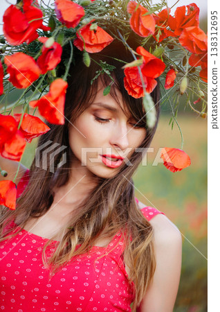 A vertical close-up portrait of a beautiful young woman with long dark hair, wearing a red patterned dress and a large wreath of red poppies, 138312695
