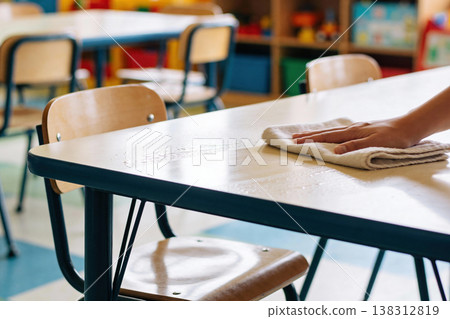 Hand wiping a classroom table with a cloth, ensuring a clean learning environment for children 138312819