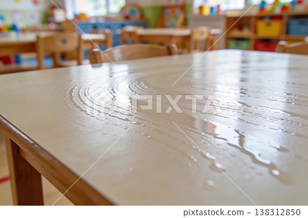 Cleaning a wooden table in a bright, empty classroom with sunlight streaming in 138312850