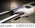 Hand wearing white glove cleaning stainless steel railing with microfiber cloth 138313123