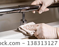 Hands wearing gloves cleaning a chrome grab bar in a bathroom with a cloth 138313127