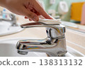 Close-up of a hand cleaning a shiny chrome faucet with a white wipe in a bathroom 138313132