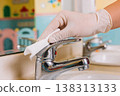 Hand wearing glove wipes down a chrome faucet with a white cloth in a bathroom 138313133