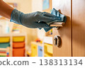 Gloved hand cleaning a door handle with a blue microfiber cloth for hygiene and disinfection 138313134