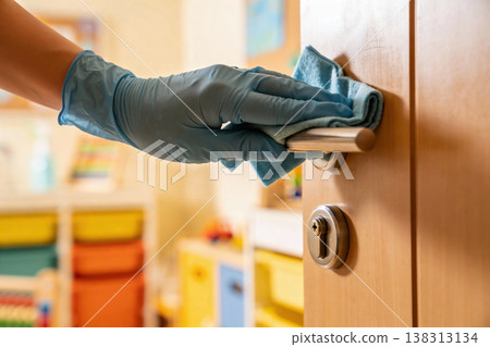 Gloved hand cleaning a door handle with a blue microfiber cloth for hygiene and disinfection 138313134