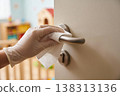 Hand wearing glove cleaning door handle with disinfectant wipe for hygiene and safety 138313136