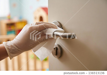 Hand wearing glove cleaning door handle with disinfectant wipe for hygiene and safety 138313136