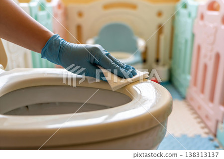 Hand wearing blue glove cleaning toilet seat with wet wipe for hygiene and sanitization 138313137