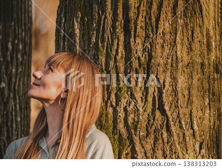 Peaceful Young Woman Leaning Against Tree 138313203