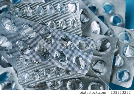 Stack of empty silver pill blister packs sits against blue background. Pharmaceutical packaging waste, empty blister packs, medical plastic recycling. 138313252