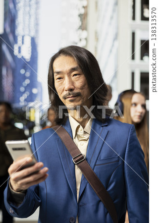 Portrait of asian businessman scrolling on phone among pedestrians in a downtown street, showing multicultural crowd, blurred motion and realistic routine of active urban environment. Portrait of asian businessman scrolling on phone among pedestrians in a downtown street, showing multicultural crowd, blurred motion and realistic routine of active urban environment. 138313570