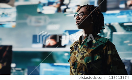 Military officer oversees mission control on digital display showing intelligence feeds. Soldier stands in front of command screens used for surveillance and threat monitoring, camera B 138313574