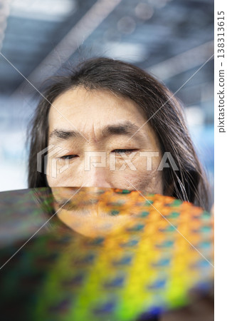 Close up of Asian man looking at silicon wafer electronic component in industrial plant. Senior manager analyzing semiconductor substrates, concept of high tech engineering Close up of Asian man looking at silicon wafer electronic component in industrial plant. Senior manager analyzing semiconductor substrates, concept of high tech engineering 138313615