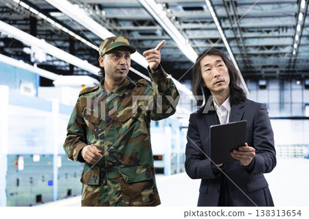 Military man and senior manager manufacturing semiconductors to win chip war, using tablet. Industrial plant director and soldier using device to inspect silicon wafers used in army defense equipment 138313654