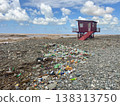 Polluted pebble beach with debris near lone lifeguard hut under clouds. 138313750