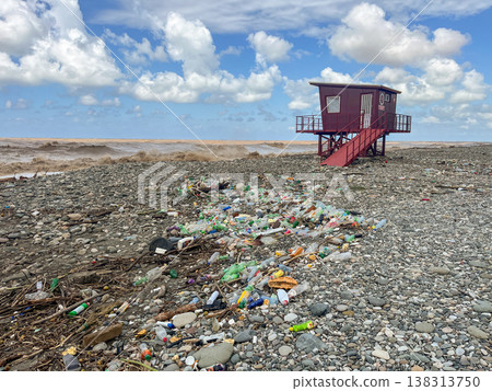 Polluted pebble beach with debris near lone lifeguard hut under clouds. Polluted pebble beach with debris near lone lifeguard hut under clouds. 138313750