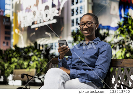 Portrait of smiling student on park bench pleased after receiving good news message on phone of positive school grade. Jolly young girl outside satisfied by high exam marks notification on smartphone Portrait of smiling student on park bench pleased after receiving good news message on phone of positive school grade. Jolly young girl outside satisfied by high exam marks notification on smartphone 138313760