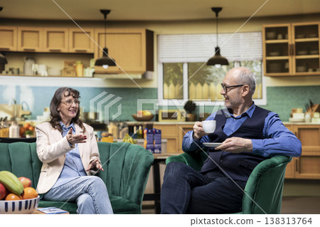 Smiling senior couple, relaxing on sofa, retired husband and wife, companionship and laughter, bonding at home, safety and wellbeing, authentic everyday life, leisure in old age. 138313764