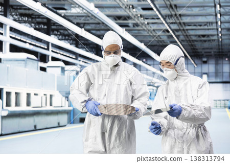 Team of manufacturing experts working together to inspect semiconductor substrate components. Teamworking cleanroom colleagues verifying optical lithography patterns on silicon wafer disk 138313794