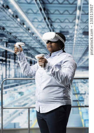 Woman reviews microchips factory hardware with VR goggles gear on platform. African american businesswoman uses virtual reality to monitor automated semiconductor production in industry 4.0 plant Woman reviews microchips factory hardware with VR goggles gear on platform. African american businesswoman uses virtual reality to monitor automated semiconductor production in industry 4.0 plant 138313987