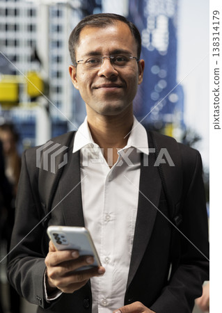Portrait of indian male professional moving past city buildings near multicultural crowd of pedestrians, capturing dynamic activity and everyday rhythm of metropolis with modern lifestyle. 138314179