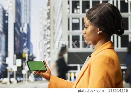 Horizontal chroma key on smartphone held by black female adult in crowded downtown area. City movement, group of multicultural pedestrians walking outdoors in the business district. Horizontal chroma key on smartphone held by black female adult in crowded downtown area. City movement, group of multicultural pedestrians walking outdoors in the business district. 138314236