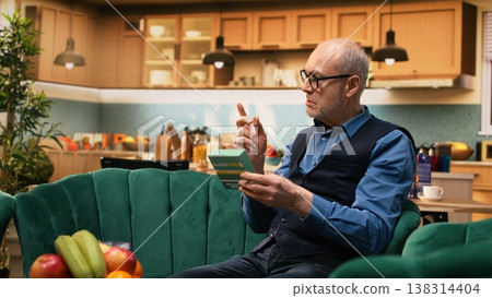 Elderly man putting on glasses to aid him in reading pills box label, ensuring correct dosage for vitality and wellbeing. Aged husband and wife doing their healthcare at home, prescription info. Elderly man putting on glasses to aid him in reading pills box label, ensuring correct dosage for vitality and wellbeing. Aged husband and wife doing their healthcare at home, prescription info. 138314404