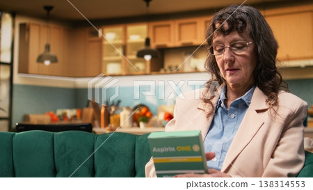 Old woman reading label on box of pills for daily healthcare routine. Checking prescribed dosage of medicine for elderly care and in-home medical support, responsible disease management. Old woman reading label on box of pills for daily healthcare routine. Checking prescribed dosage of medicine for elderly care and in-home medical support, responsible disease management. 138314553