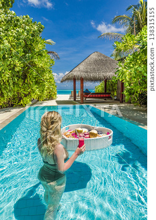 Luxury resort swimming pool with floating breakfast tray in heart shape, blonde woman relaxing, romantic honeymoon vacation tropical beach background 138315155