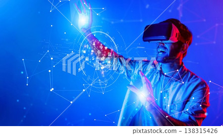 Young man exploring virtual reality with immersive goggles, interacting with holographic projections and futuristic digital interface elements in vibrant blue tones. Raster 138315426