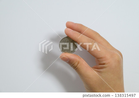 一手拿著一枚100日圓硬幣，周圍是空曠的空間。 138315497